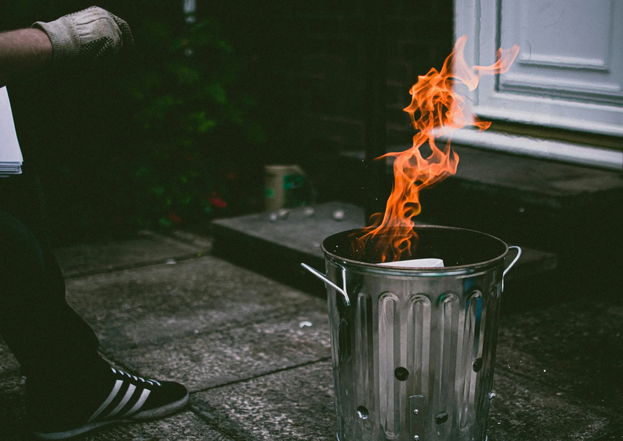 A stainless steel trash can outside with flames and smoke, creating a dramatic scene.